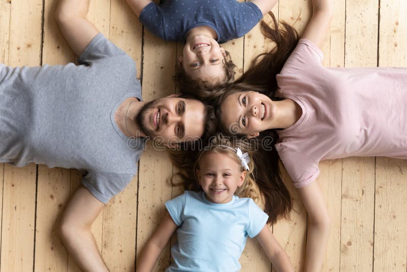 Above view couple and kids lying on wooden warm floor. Above view beautiful couple and little kids lying on wooden warm floor holding hands smiling looking at stock photo