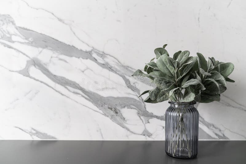  artificial plant in glass vase on gray spray-painted  working table with  marble wall in the background /apartment interi royalty free stock photo