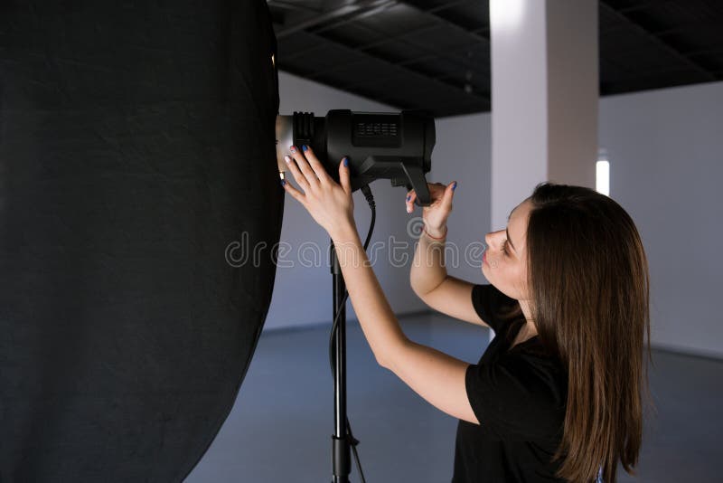 Assistant of photographer adjust light in studio. Beautiful woman with camera is setting photographing equipment getting ready for a photo shoot stock photography