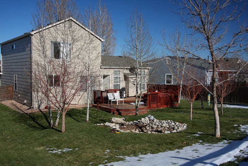 Back of two-story house in winter. Back of a two-story modern house with scattered snow and bare trees in backyard. Redwood deck and jacuzzi are also in the stock photography