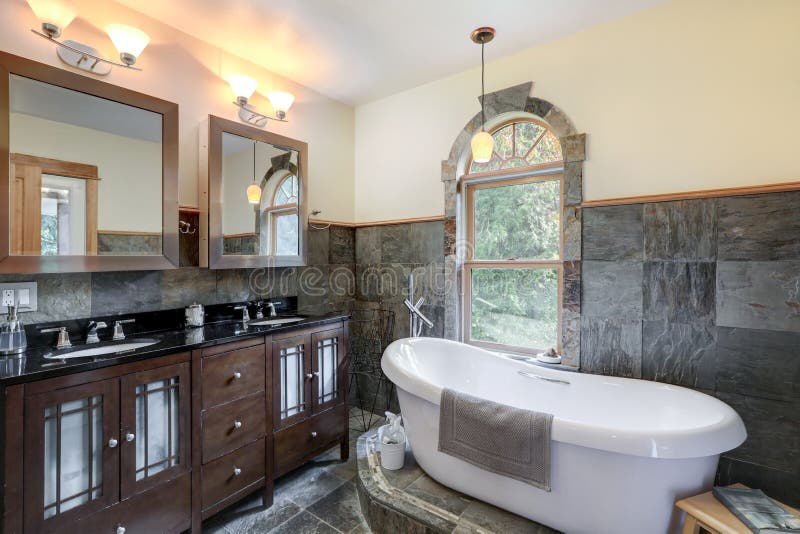 Bathroom interior with grey tiles and free standing white tub with dark wood classic vanity. With black countertop and two mirrors royalty free stock photo