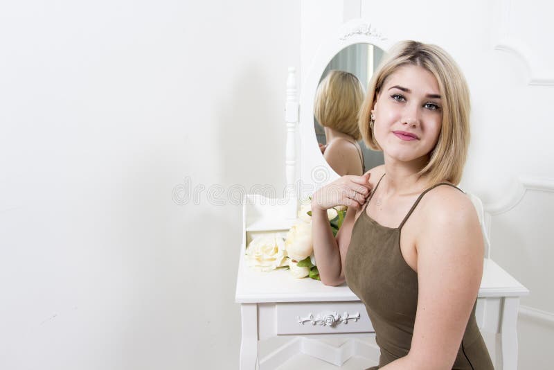 Beautiful attractive blonde girl sits in front of a mirror in the bedroom. Young woman in dressing room. stock image