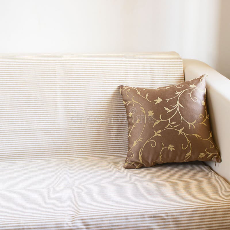 Beautiful brown pillow on light sofa covered by linen blancet with pale stripes on the background of white wall. Decoration in. Beautiful brown pillow on light stock image