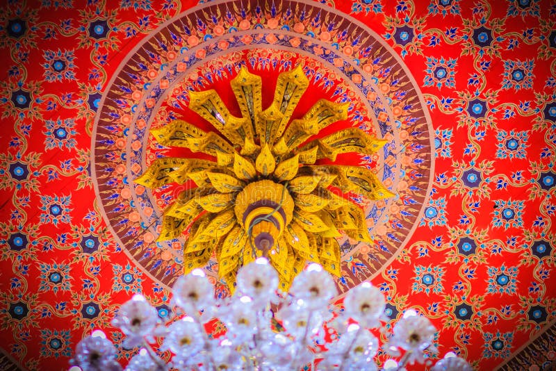 Beautiful chandelier lamp is hanging on the decorated ceiling in. The Buddhist church, Thailand. Colorful pattern of ceiling with decorative chandelier lamp stock image