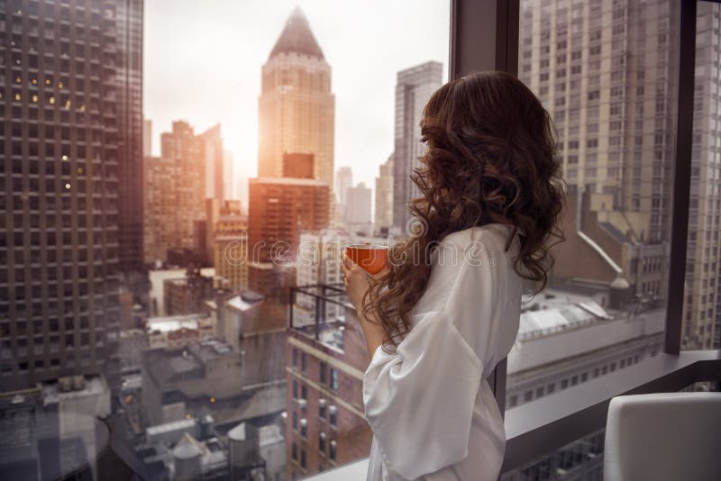 Beautiful woman holding coffee cup and looking to the window in luxury Manhattan penthouse apartments royalty free stock photos