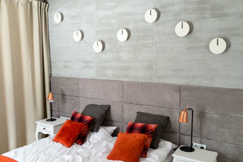Bedroom with a large bed, orange pillows arranged in a row, wall covered with gray material, visible tables and bedside lamps. royalty free stock photos
