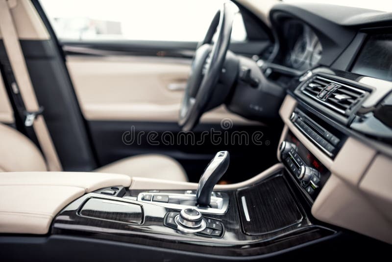 Beige and black interior of modern car, close-up details of automatic transmission and gear stick against steering wheel ba. Modern beige and black interior of stock photo