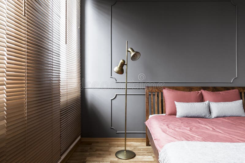Blinds and golden lamp in dark and elegant bedroom interior with. Pink sheets on a wooden bed and molding on the wall. Real photo royalty free stock photography