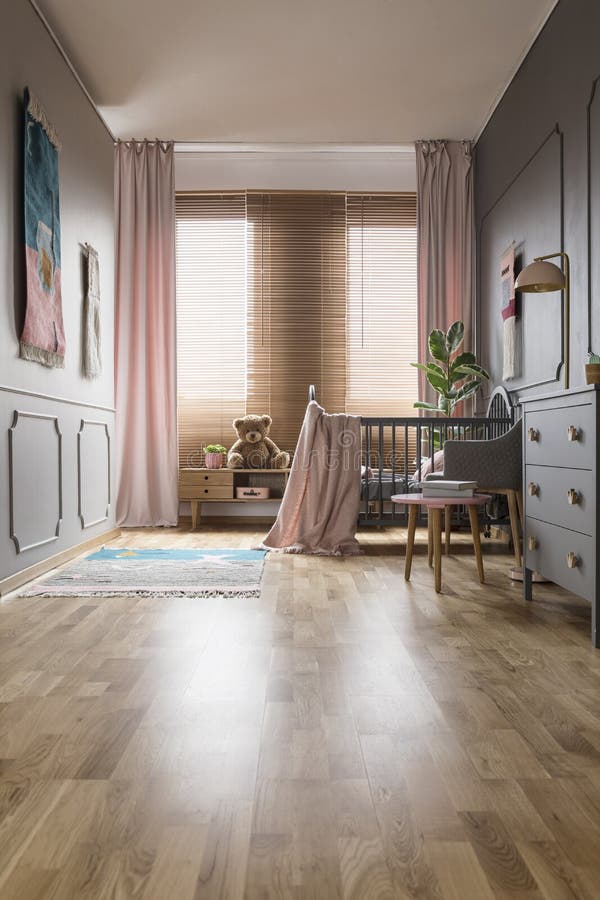 Blinds in spacious child`s bedroom with pink drapes and grey cab. Inet near bed with blanket. Real photo royalty free stock image