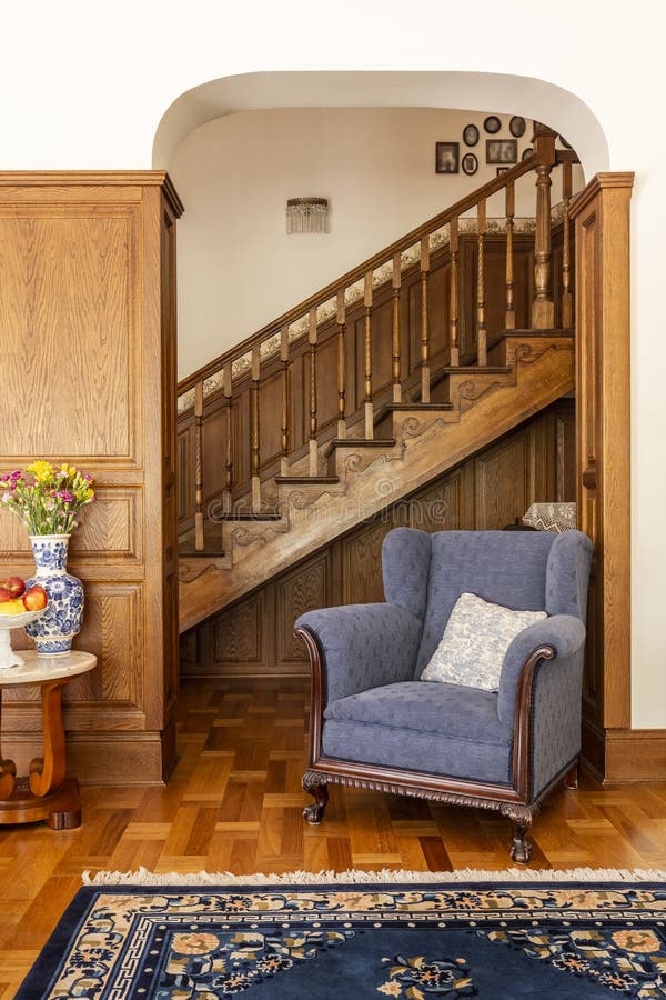 Blue armchair against wooden stairs in classic living room inter. Ior with flowers and carpet. Real photo stock photo