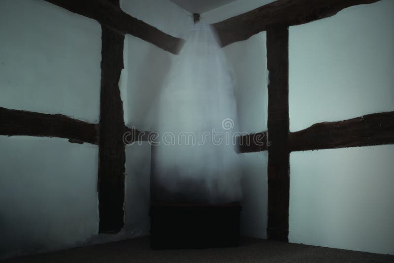 A blurred ghost floating above a metal box in a corner of an old timber framed building.  royalty free stock photo