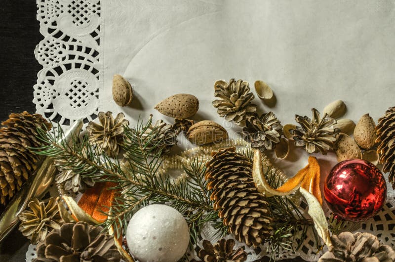 Bottom edge of the openwork paper napkin with various pine cones, fir branch,Christmas toys, almonds and orange peel on black back stock images