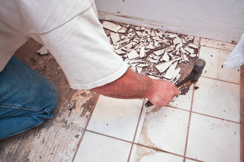 Breaking up floor tiles. A tile setter uses a hammer to break up ceramic floor tiles in a bathroom. This laborer is demolishing the flooring in preparation for royalty free stock photo