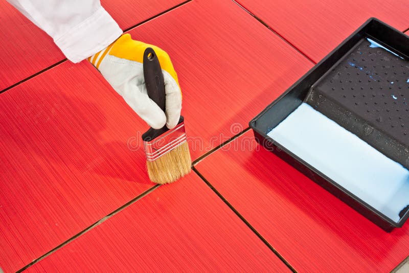Brush primer grout of red tiles resistant. Hand in yellow glove painting with black brush primer on grout of red tiles resistant royalty free stock photography