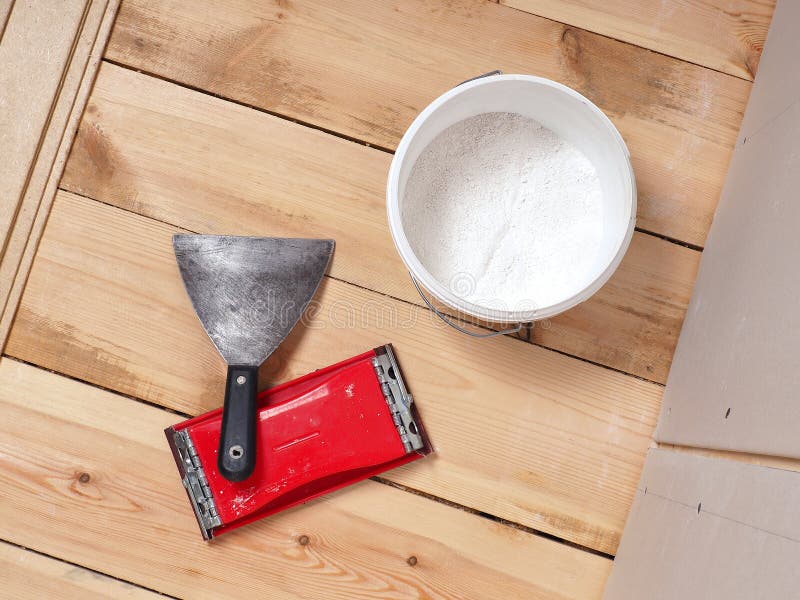 A bucket of putty, a spatula and an emery grater lie on the floor. Nearby is a wall of drywall and lie fiberboard. The floor of. Boards stock photos
