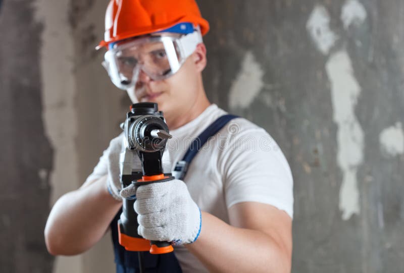 The builder with hammer drill perforator equipment making hole in wall at construction site. Repair work, interior decoration of stock image