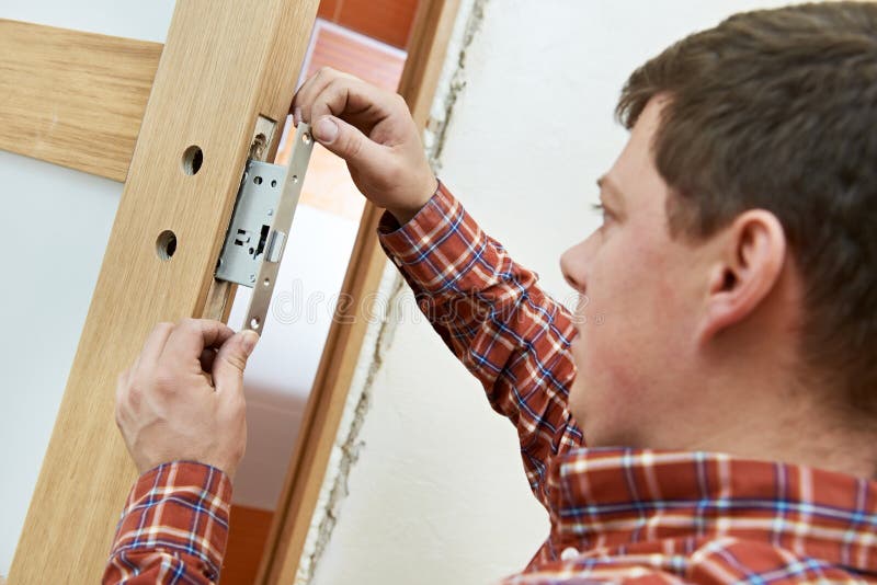 Carpenter at door lock installation. Male handyman carpenter at interior wood door lock installation royalty free stock photo