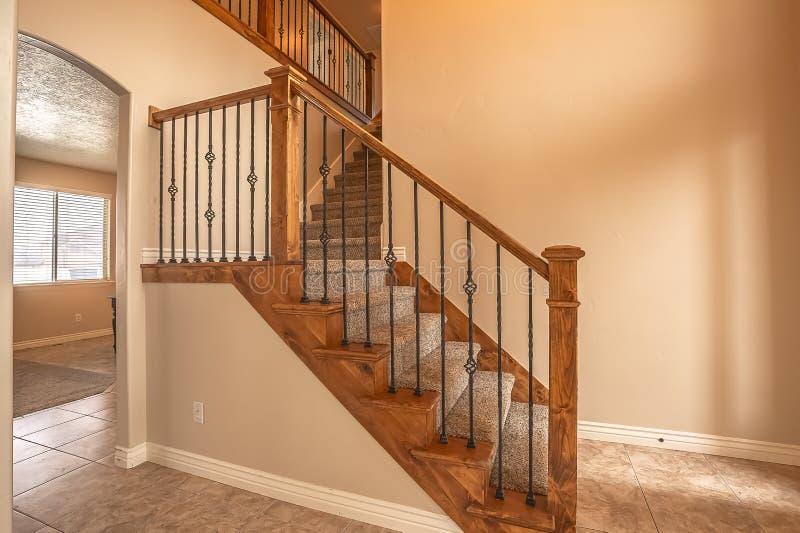 Carpeted stairs with wood handrail and metal railing inside an empty new home. Beige wall, shiny floor, window with blinds, and arched doorway can also be seen stock photography