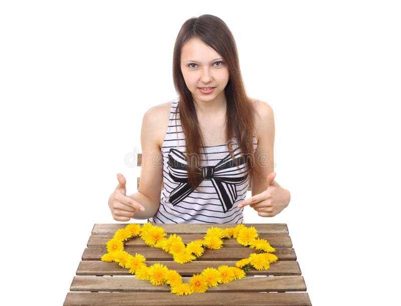 Caucasian teen girl, 15 years old, shows a yellow. Caucasian teen girl, brunette, 15 years old, shows a yellow valentine made from dandelion flowers on the table royalty free stock photography