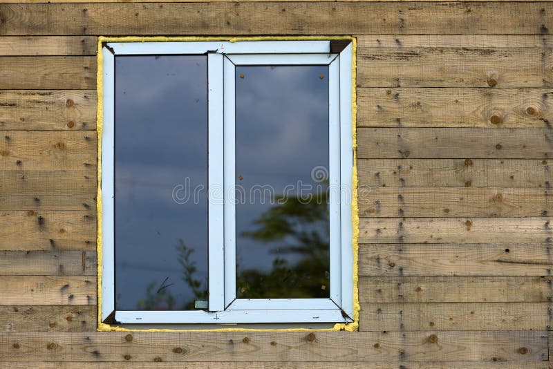 Close-up detail of new narrow plastic vinyl window installed in. House wall of brown natural wooden planks and boards. Real estate property, comfortable cottage stock image