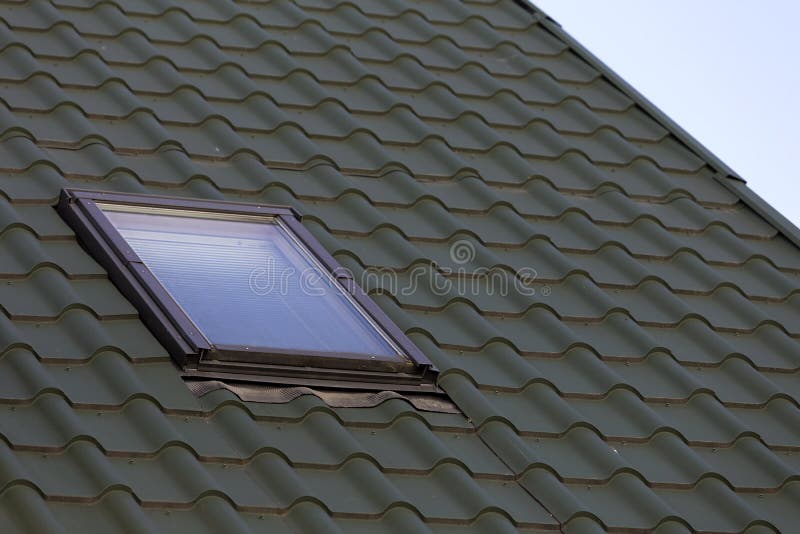 Close-up detail of new small attic plastic window installed in d. Ark green shingled house roof background. Professionally done building and construction work stock photo