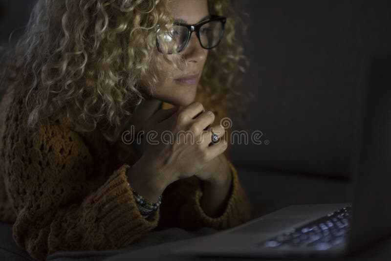 Close up portrait of people and technology in the dark light - woman look the screen of personal laptop computer by night lay down royalty free stock photo