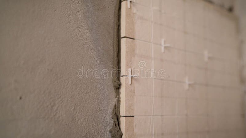 Close-up view of tiler hands fixing wall tile with spacers at home repair renovation work. Laying tiles on the wall stock images