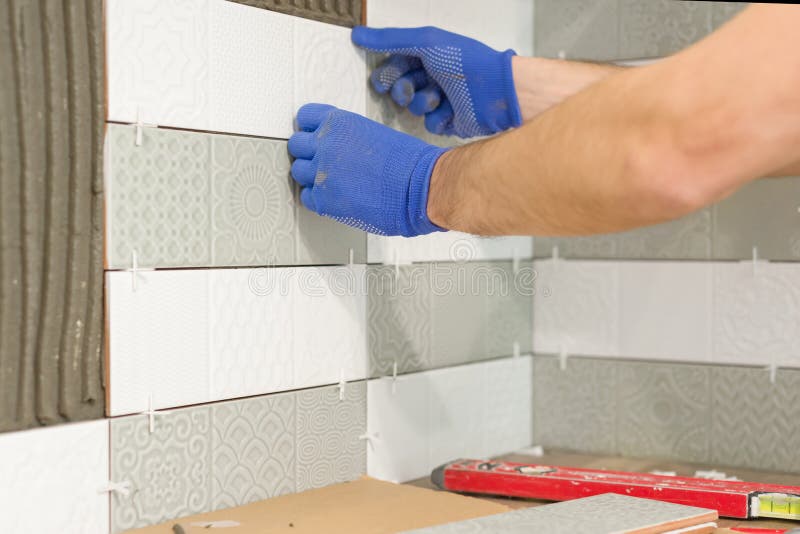 Closeup of tiler hand laying ceramic tile on wall in kitchen, renovation, repair, construction stock images