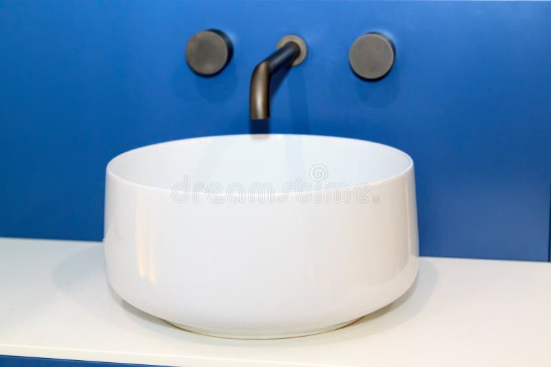 closeup view of white sink with modern simple faucet mounted in blue wall stock photography