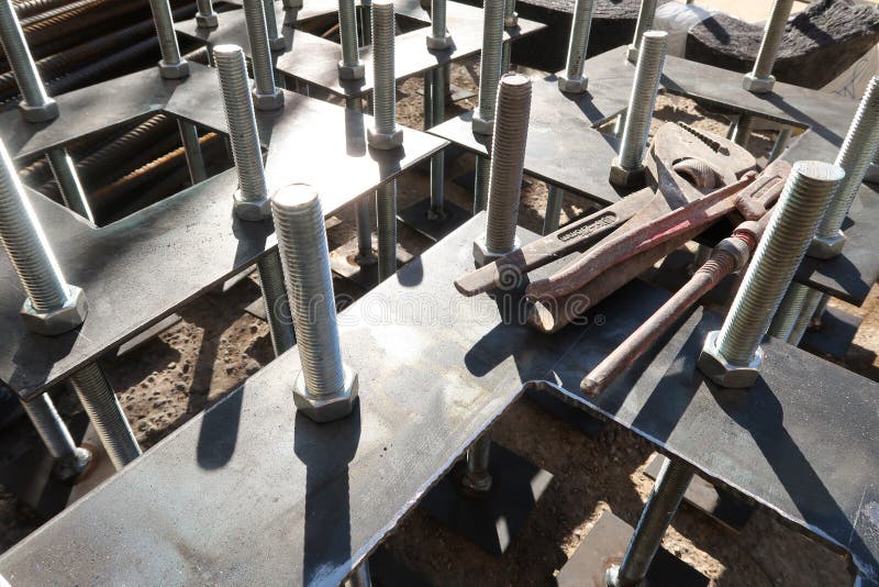 Construction site for a building with a steel structure. Plates with anchor bolts for mounting steel columns on a reinforced. Concrete foundation. Wrenches stock images