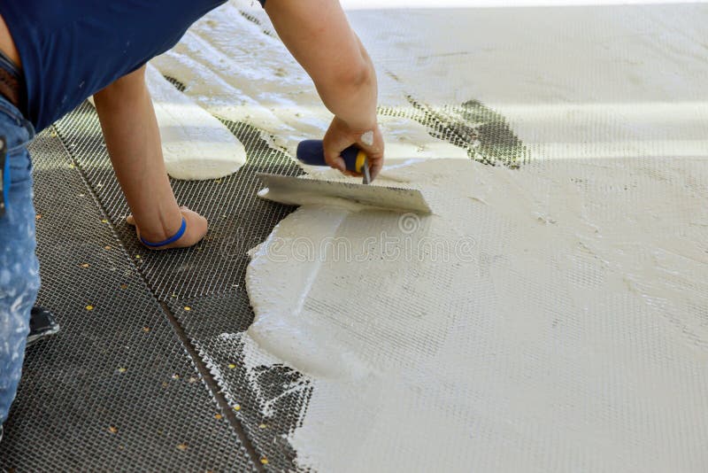 A construction worker troweling mortar onto concrete floor in preparation for laying floor tile. A construction worker troweling mortar onto a concrete floor in stock image