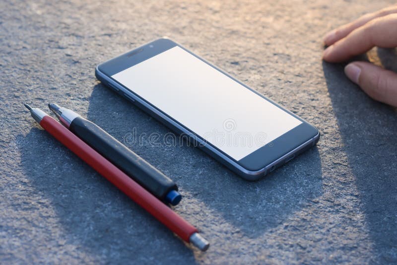 Contemporary modern smartphone on stone finishing background. Pencils and hand. Visual effects. Blank display replaceable with needed design.Vertical mockup stock image