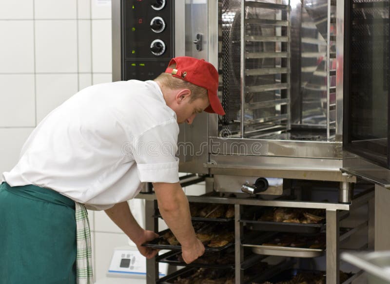 Cook at commercial stove. A professional stove (oven) used in a commercial kitchen for preparing large amounts of food. The cook operating the machine stock image