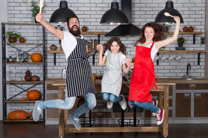 Cooking with child might be fun. Having fun in kitchen. Family mom dad and little daughter wear aprons jump in kitchen stock images