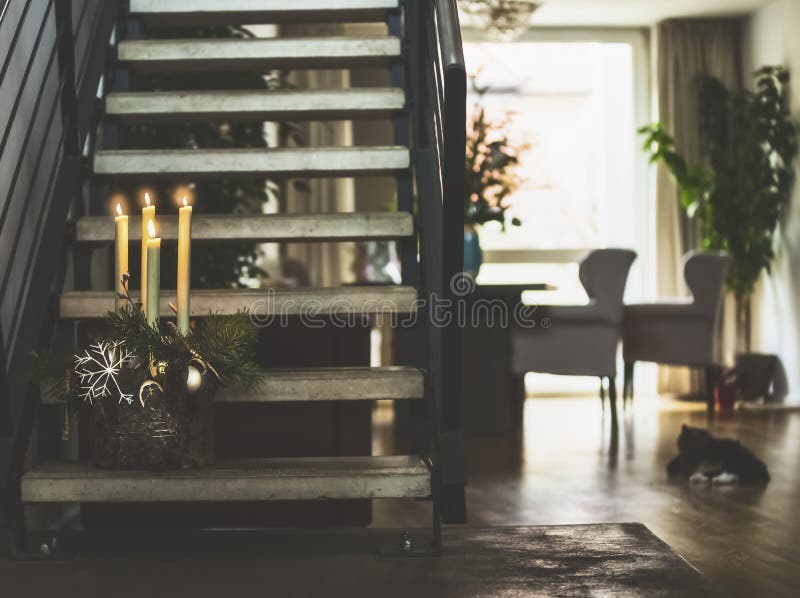 Cozy living room with stairs to second floor , winter decoration with burning candles on steps, window and cat. Winter holidays. Cozy living room with stairs to royalty free stock images