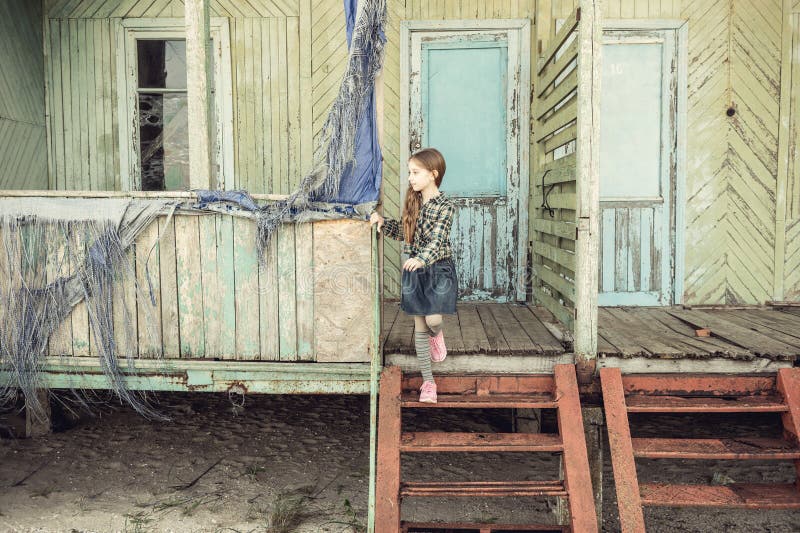 Cute little girl standing on stairs of abandoned wooden house. At a seaside royalty free stock photo