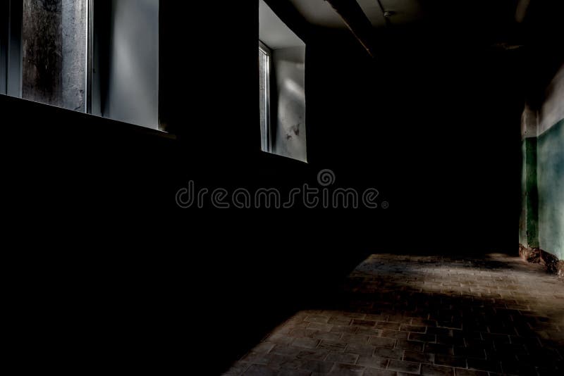 A dark corridor with two rectangular windows, dim daylight illuminates a part of the wall and the floor surface with a tile stock photo
