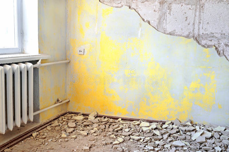 Destroyed dirty empty yellow interior with vintage radiator. Repair of apartments with old rusty cast iron central heating radiator or battery and old grungy stock photography