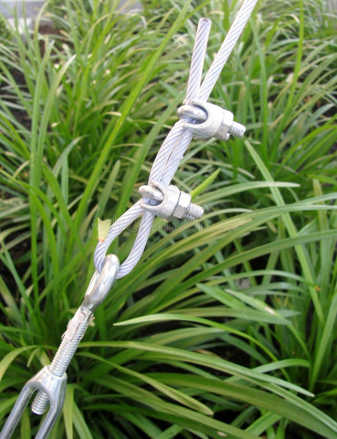 Detail off the cable end. Steel turnbuckle holding hook eye with fastening and metal cables against green grass royalty free stock images
