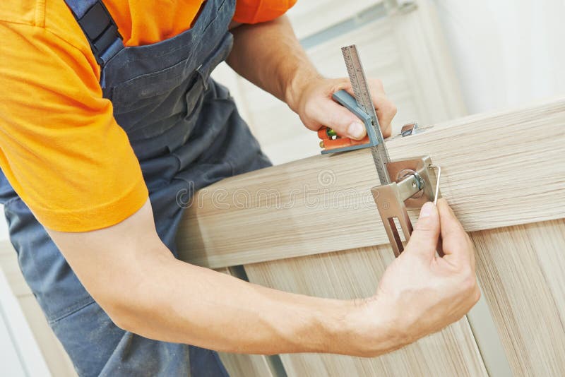 Door lock installation. Close-up carpenter hands with doorlock during lock process installation into wood door stock photography