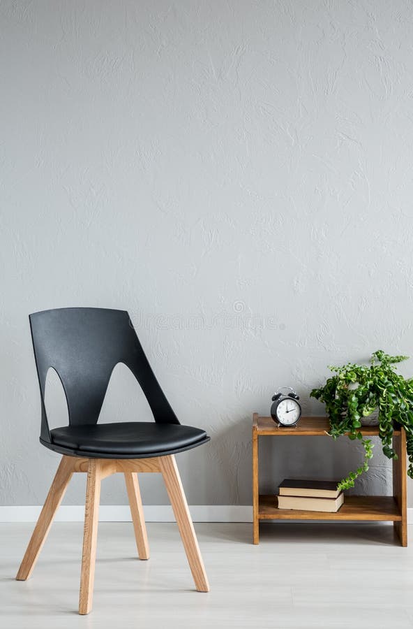 Elegant black wooden chair next to cabinet with clock and flowers in modern office interior royalty free stock photography