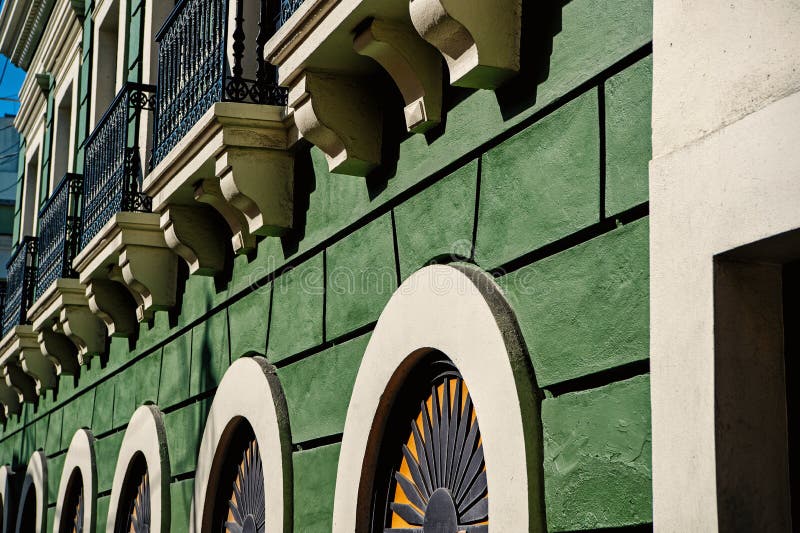 Facade wall on green plastered background in San Juan, Puerto Rico. House with windows and decorative balconies. Symmetry and urban geometry concept royalty free stock images