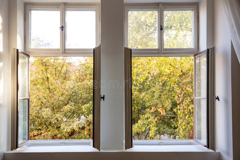 Fall season. Trees with autumn leaves out of two open white wooden windows. Fall, autumn season. Trees with yellow leaves out of two open white wooden windows stock images