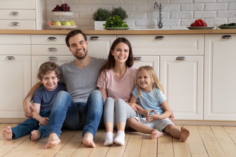 Family with kids hugging sitting on warm floor in kitchen. Family with little kids hugging sit on warm floor leaned on kitchen cabinet built-in furniture look at royalty free stock photography