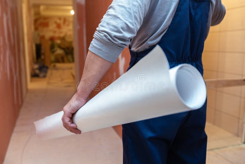 Worker is holding the white wallpaper roll before gluing in apartment is inder construction, remodeling, renovation royalty free stock image