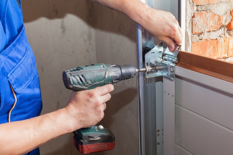 Garage doors installation.Worker installing lifting system in metal profil with screwdriver. royalty free stock images