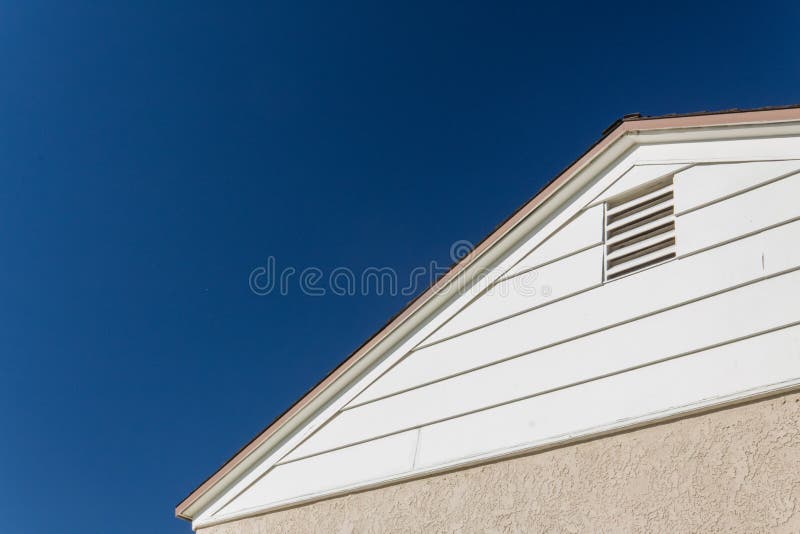 Generic house view of side and roof edge, stucco and vinyl with attic ventilation set against a deep blue sky stock image