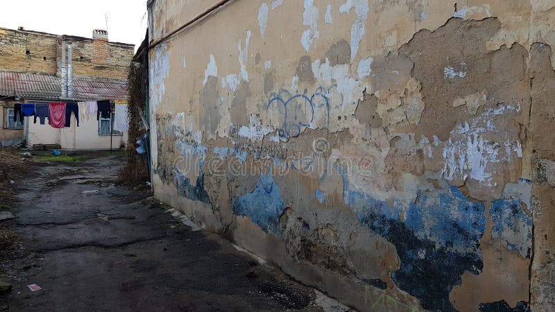 Old rough stone wall surface of ruined building with dirty flaking plaster. Ghetto court yard with hanging laundry clothes and weathered wall on foreground royalty free stock image