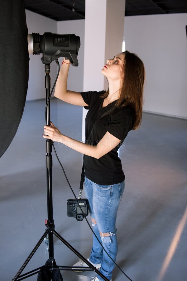 Girl photographer adjust light in studio. Beautiful woman with camera is setting photographing equipment getting ready for a photo shoot stock photos