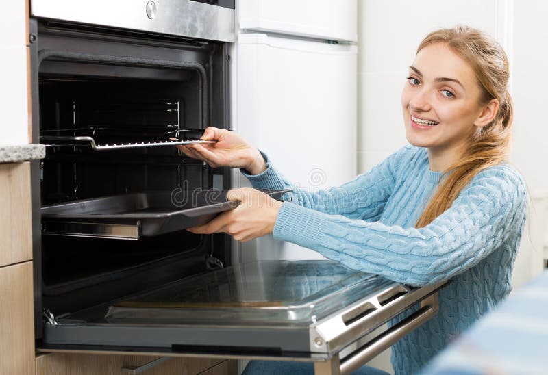 Girl putting baking tray in kitchen oven. Portrait of young girl putting baking tray in kitchen oven royalty free stock image